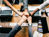 People fist pumping sitting at a table alongside their laptops